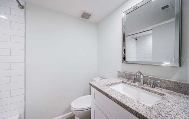 bathroom featuring a tile shower, vanity, and toilet