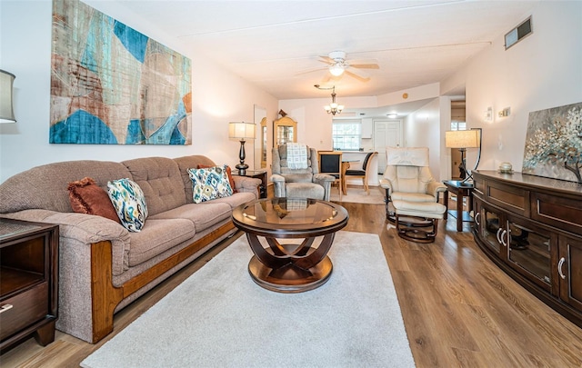 living room featuring ceiling fan with notable chandelier and light wood-type flooring