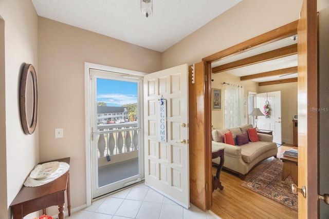 doorway with a textured ceiling, light hardwood / wood-style floors, and beamed ceiling