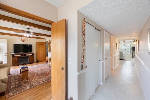 corridor featuring light wood-type flooring, a textured ceiling, and beam ceiling