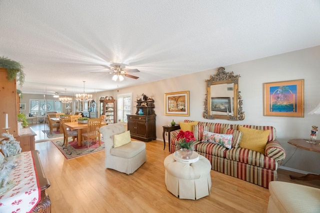 living room featuring ceiling fan with notable chandelier, light hardwood / wood-style flooring, and a textured ceiling