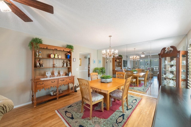 dining space with ceiling fan with notable chandelier, a textured ceiling, and light hardwood / wood-style flooring