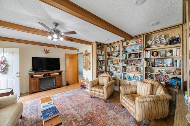 living room with ceiling fan, a textured ceiling, light hardwood / wood-style floors, and beam ceiling