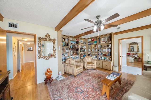 living room featuring beamed ceiling, a textured ceiling, light hardwood / wood-style floors, decorative columns, and ceiling fan