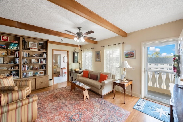 living room with ceiling fan, a wealth of natural light, light hardwood / wood-style floors, and beam ceiling