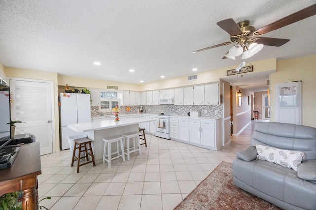 kitchen featuring white cabinets, decorative backsplash, a kitchen island, a breakfast bar, and white appliances