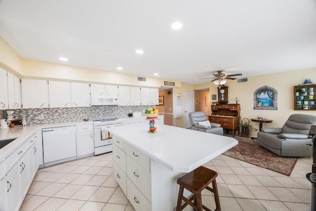 kitchen featuring white cabinetry, tasteful backsplash, a breakfast bar area, white appliances, and a center island