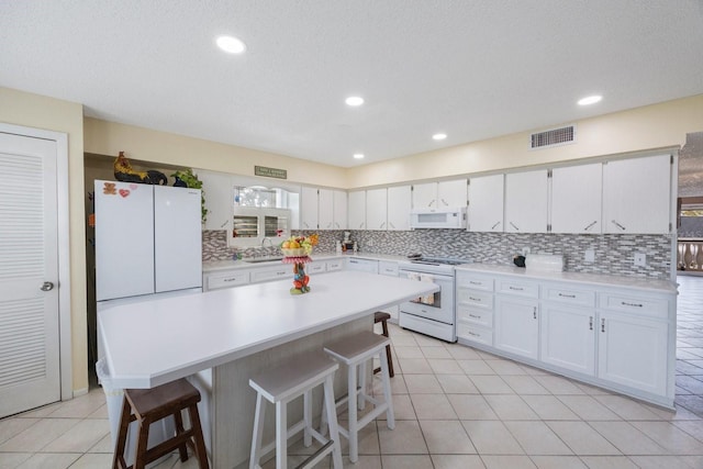 kitchen with white cabinets, a breakfast bar area, and white appliances