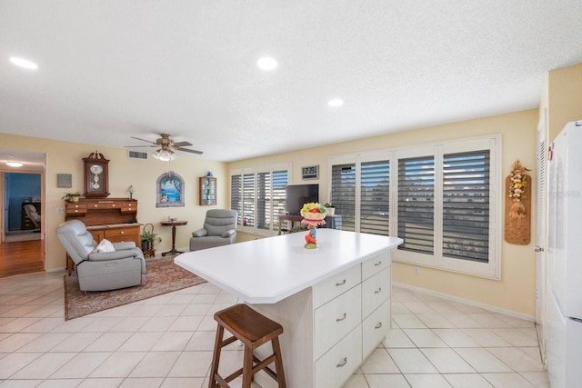 kitchen featuring a kitchen island, white refrigerator, light tile patterned floors, a kitchen breakfast bar, and white cabinets