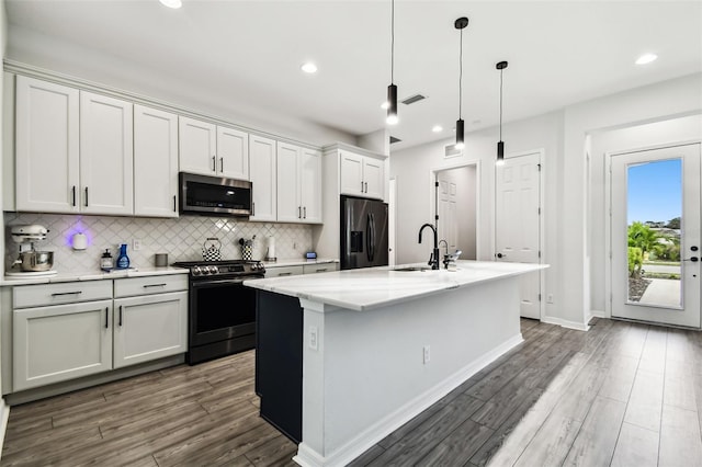 kitchen with a center island with sink, stainless steel appliances, and decorative light fixtures