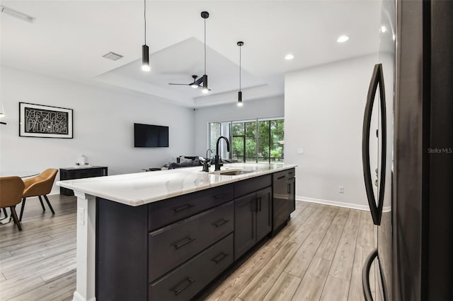 kitchen featuring stainless steel refrigerator, ceiling fan, sink, decorative light fixtures, and a kitchen island with sink