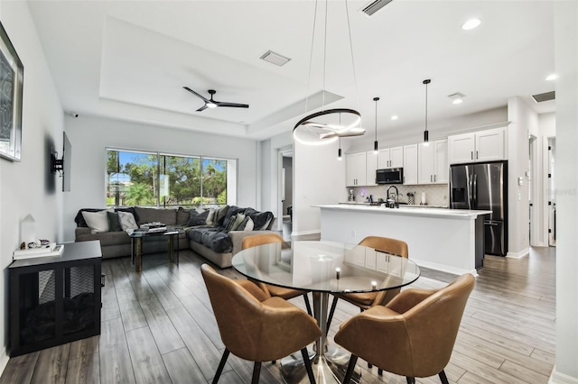 dining room featuring ceiling fan, light wood-type flooring, and a tray ceiling