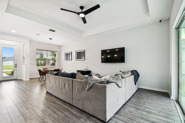 living room with a raised ceiling, ceiling fan, and light hardwood / wood-style floors