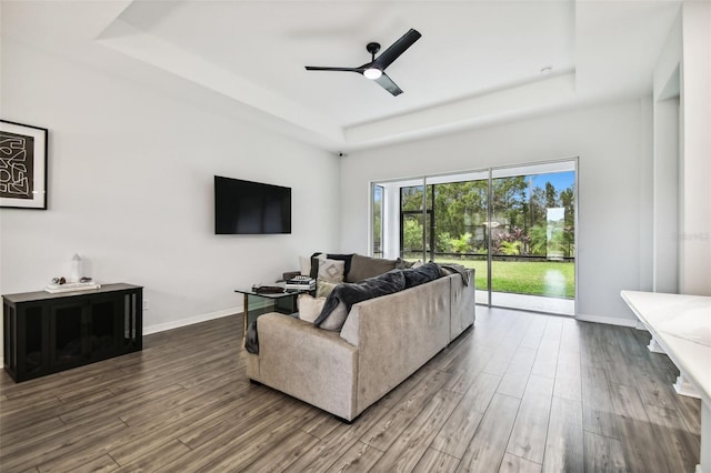 living room with wood-type flooring, a raised ceiling, and ceiling fan