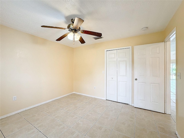 unfurnished bedroom with a textured ceiling, light tile patterned flooring, ceiling fan, and a closet