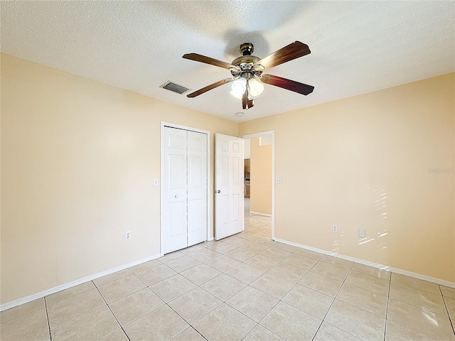 unfurnished bedroom featuring light tile patterned flooring, a closet, a textured ceiling, and ceiling fan