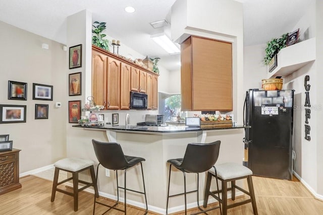 kitchen featuring light hardwood / wood-style floors, sink, black appliances, kitchen peninsula, and a breakfast bar area