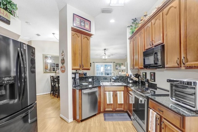 kitchen with dark stone countertops, sink, light hardwood / wood-style flooring, and appliances with stainless steel finishes