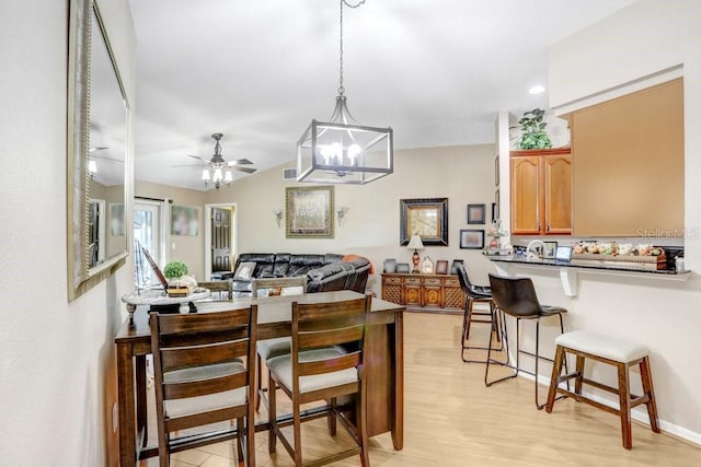 kitchen with light hardwood / wood-style floors, a breakfast bar, kitchen peninsula, ceiling fan with notable chandelier, and hanging light fixtures