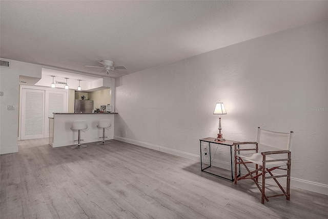 living area with ceiling fan, a textured ceiling, and light hardwood / wood-style flooring