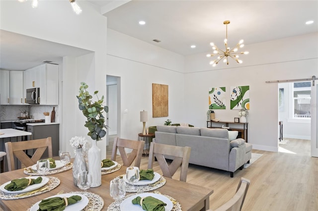 dining area with a barn door, light hardwood / wood-style flooring, and a notable chandelier