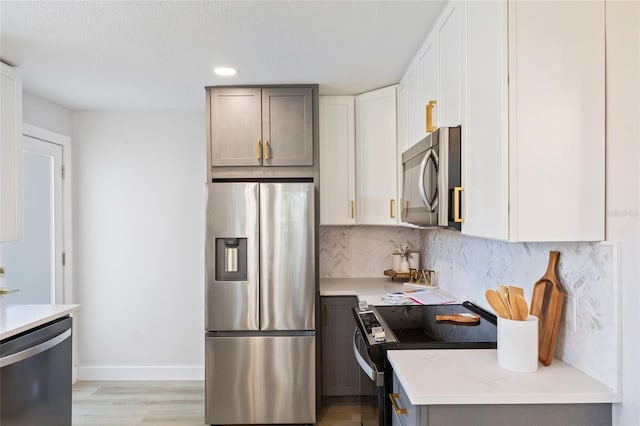 kitchen with light hardwood / wood-style flooring, gray cabinets, appliances with stainless steel finishes, light stone counters, and decorative backsplash