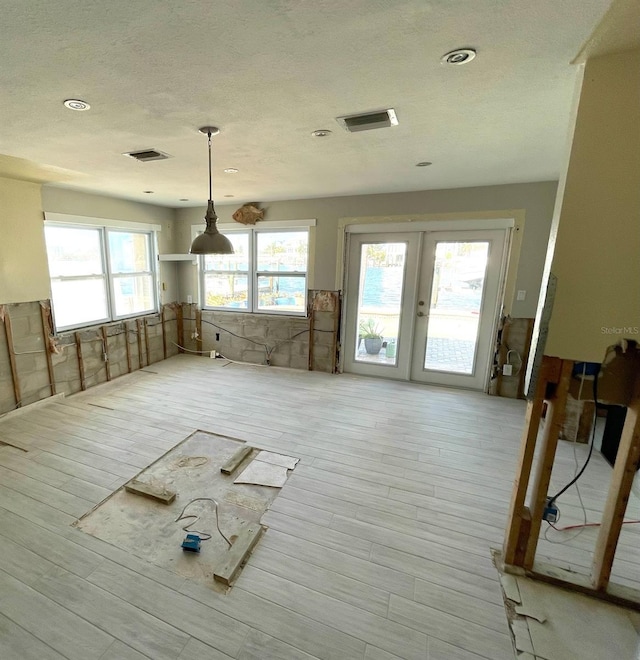 misc room featuring a textured ceiling, french doors, tile walls, and light hardwood / wood-style flooring