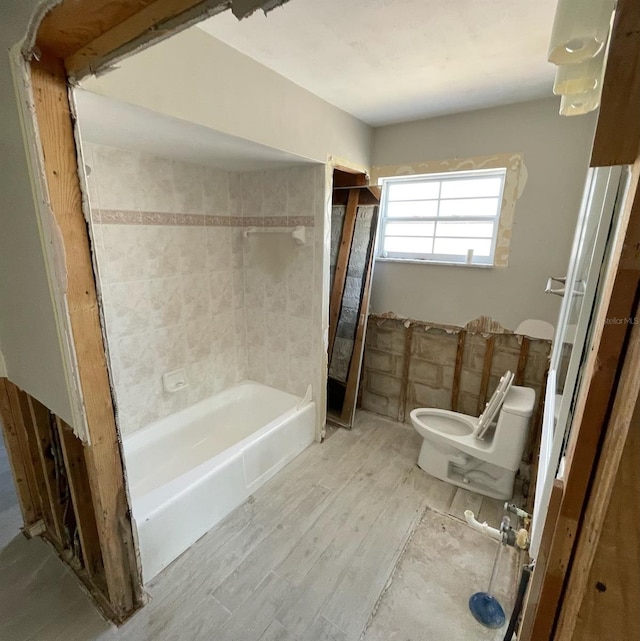 bathroom with hardwood / wood-style flooring, toilet, and tiled shower / bath