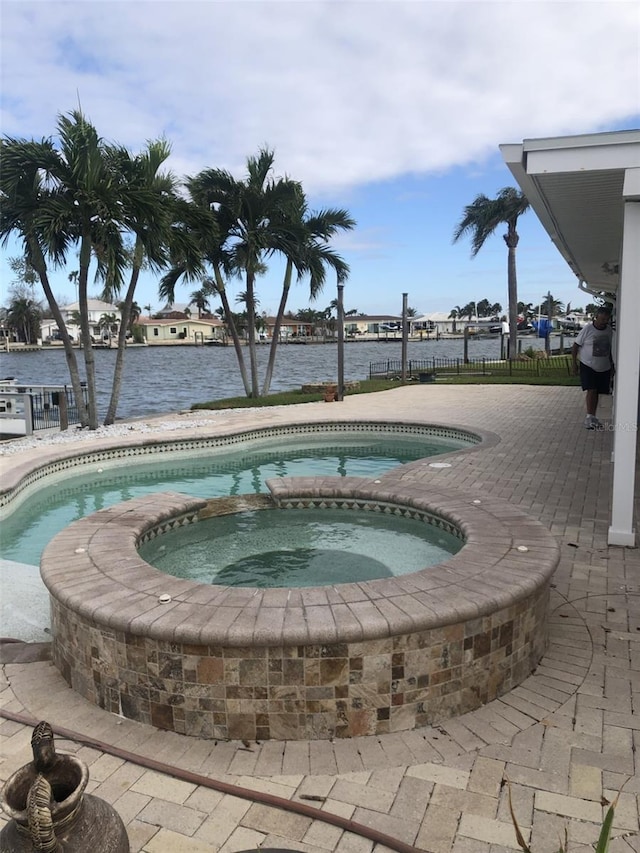 view of pool with an in ground hot tub, a water view, and a patio area