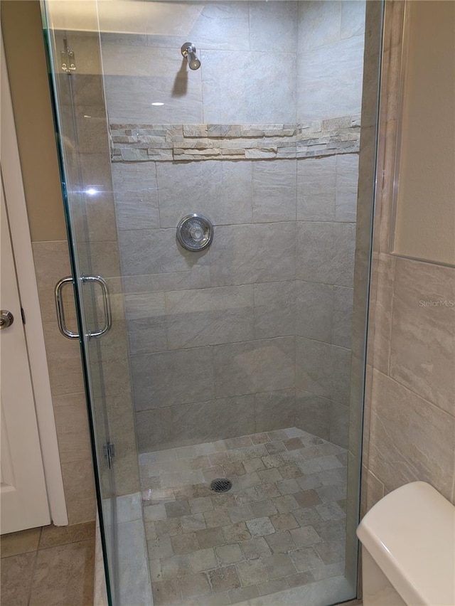 bathroom featuring toilet, an enclosed shower, and tile walls