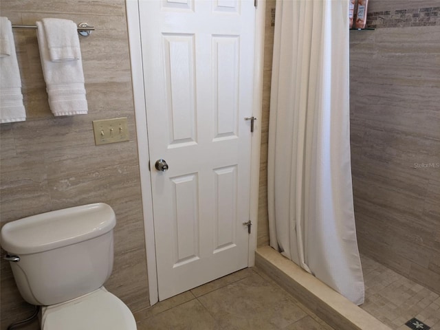 bathroom with a shower with shower curtain, tile patterned flooring, toilet, and tile walls