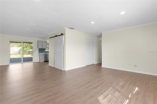 unfurnished living room featuring a barn door, light hardwood / wood-style floors, and ornamental molding