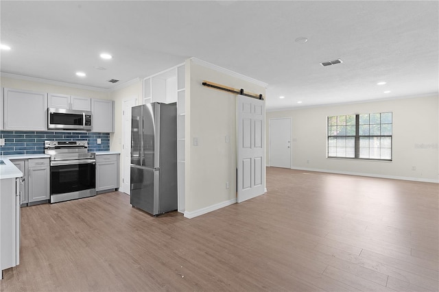 kitchen featuring crown molding, decorative backsplash, a barn door, light wood-type flooring, and appliances with stainless steel finishes