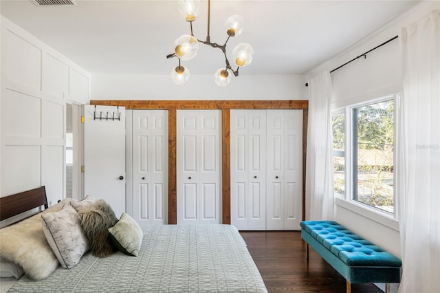 bedroom with dark wood-type flooring, an inviting chandelier, and multiple closets