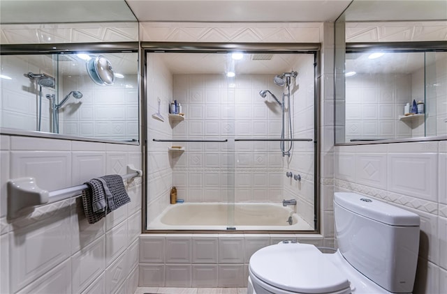 bathroom featuring tile walls, toilet, and combined bath / shower with glass door