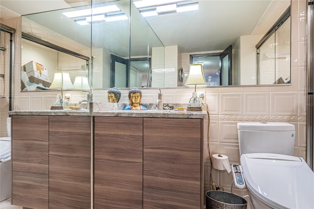 bathroom with a shower with door, vanity, tile walls, and toilet