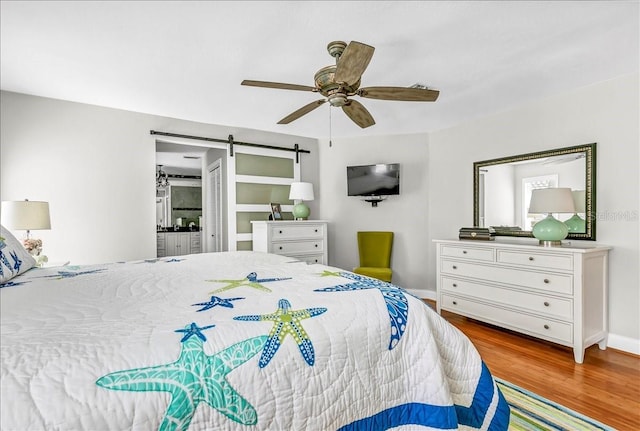 bedroom with a barn door, baseboards, ceiling fan, and wood finished floors