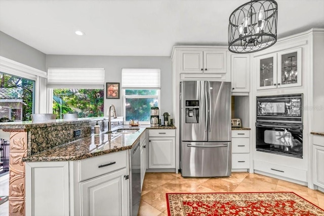 kitchen with white cabinets, dark stone counters, a peninsula, black appliances, and a sink