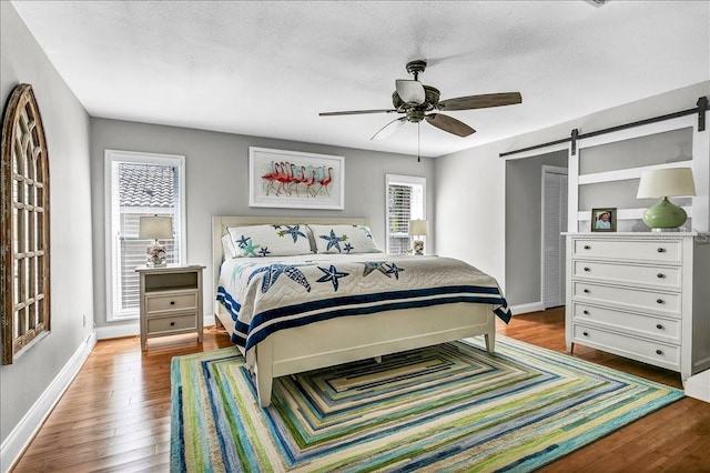 bedroom with a barn door, baseboards, ceiling fan, hardwood / wood-style floors, and a textured ceiling