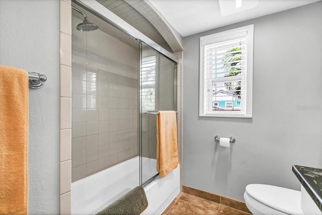 bathroom with baseboards, combined bath / shower with glass door, toilet, and tile patterned floors