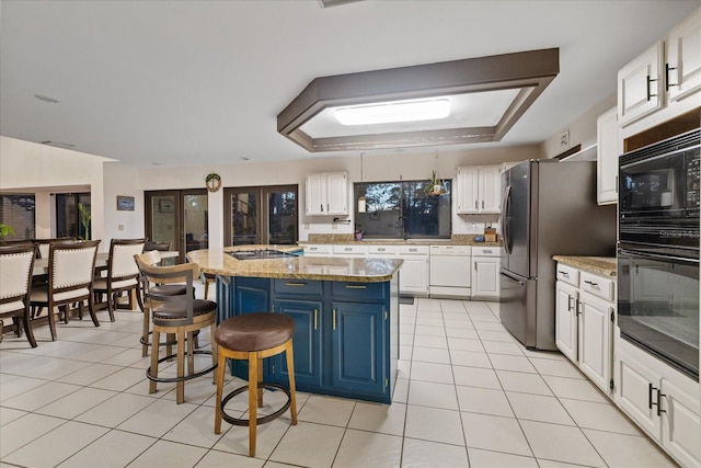 kitchen with black appliances, light stone counters, a breakfast bar area, a kitchen island, and white cabinets