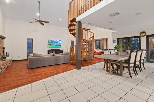 dining room with a high ceiling, ceiling fan, a brick fireplace, and light hardwood / wood-style flooring