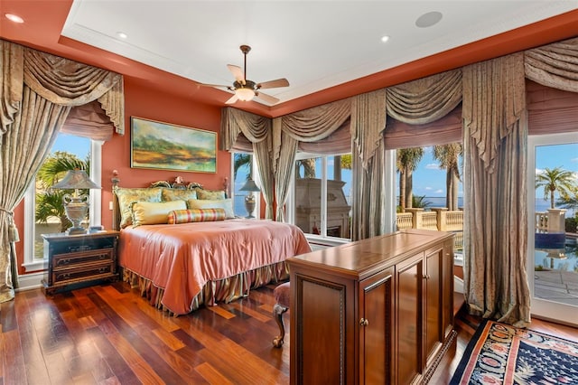 bedroom featuring a raised ceiling, access to outside, dark wood-type flooring, ceiling fan, and multiple windows