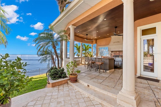 view of patio with a bar, area for grilling, a water view, a grill, and ceiling fan