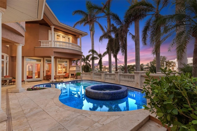 pool at dusk with an in ground hot tub and a patio area