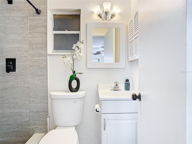 bathroom featuring a tile shower, vanity, and toilet