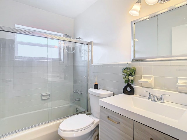 full bathroom with combined bath / shower with glass door, vanity, toilet, and tile walls