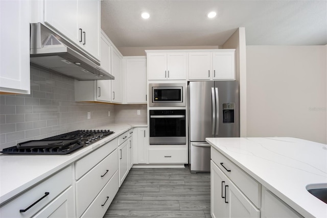 kitchen with light hardwood / wood-style floors, light stone counters, appliances with stainless steel finishes, backsplash, and white cabinets