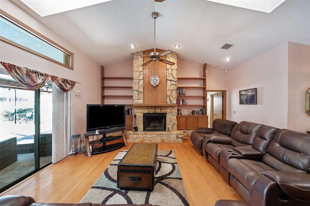 living room with vaulted ceiling with skylight, ceiling fan, light hardwood / wood-style floors, and a stone fireplace