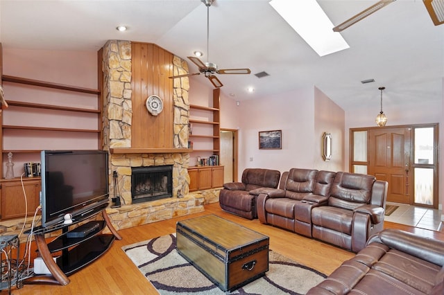 living room with light wood-type flooring, a stone fireplace, ceiling fan, and lofted ceiling